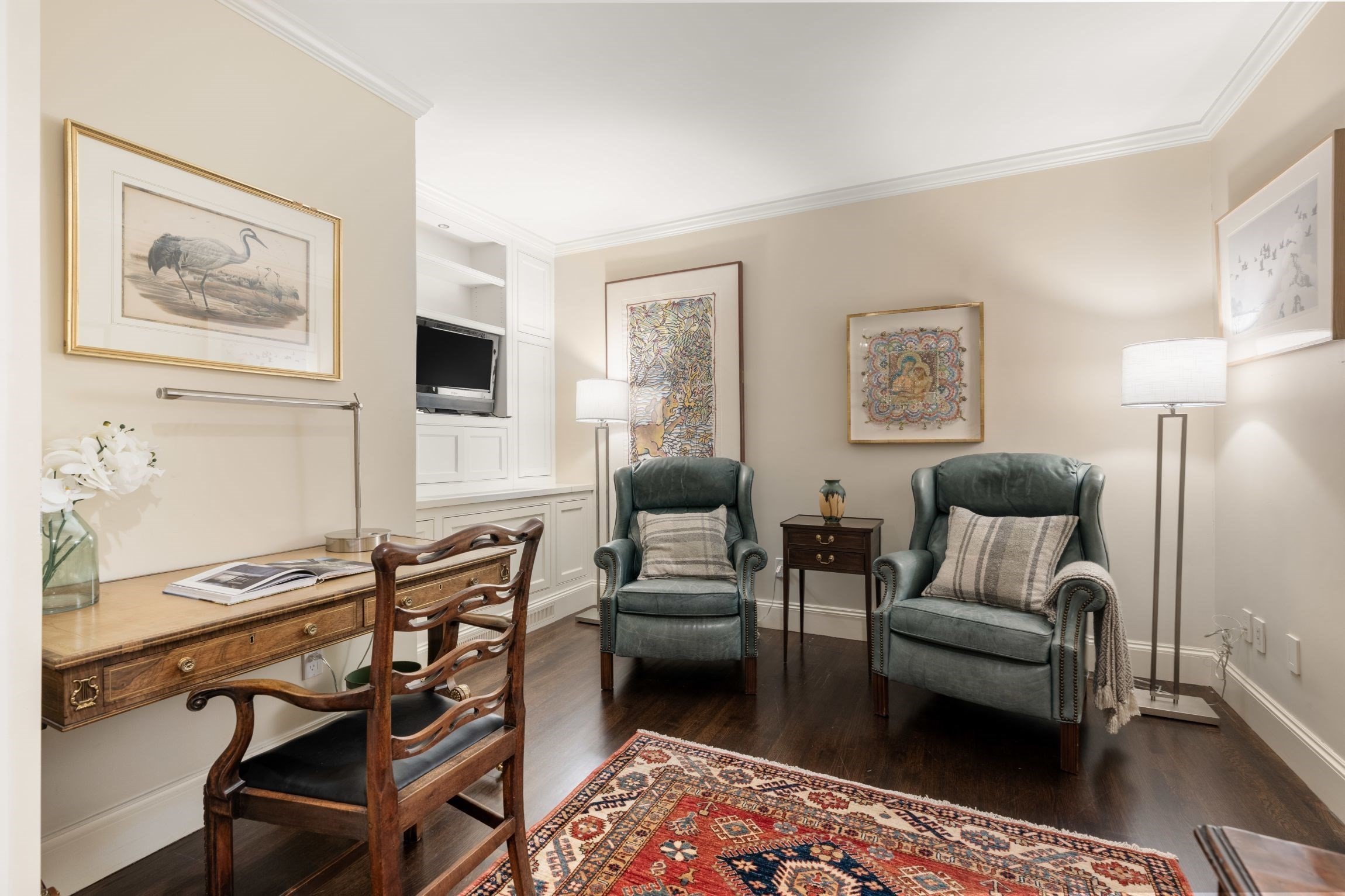 Living room with green leather armchairs, a wooden writing desk, built-in cabinetry, and a patterned rug.