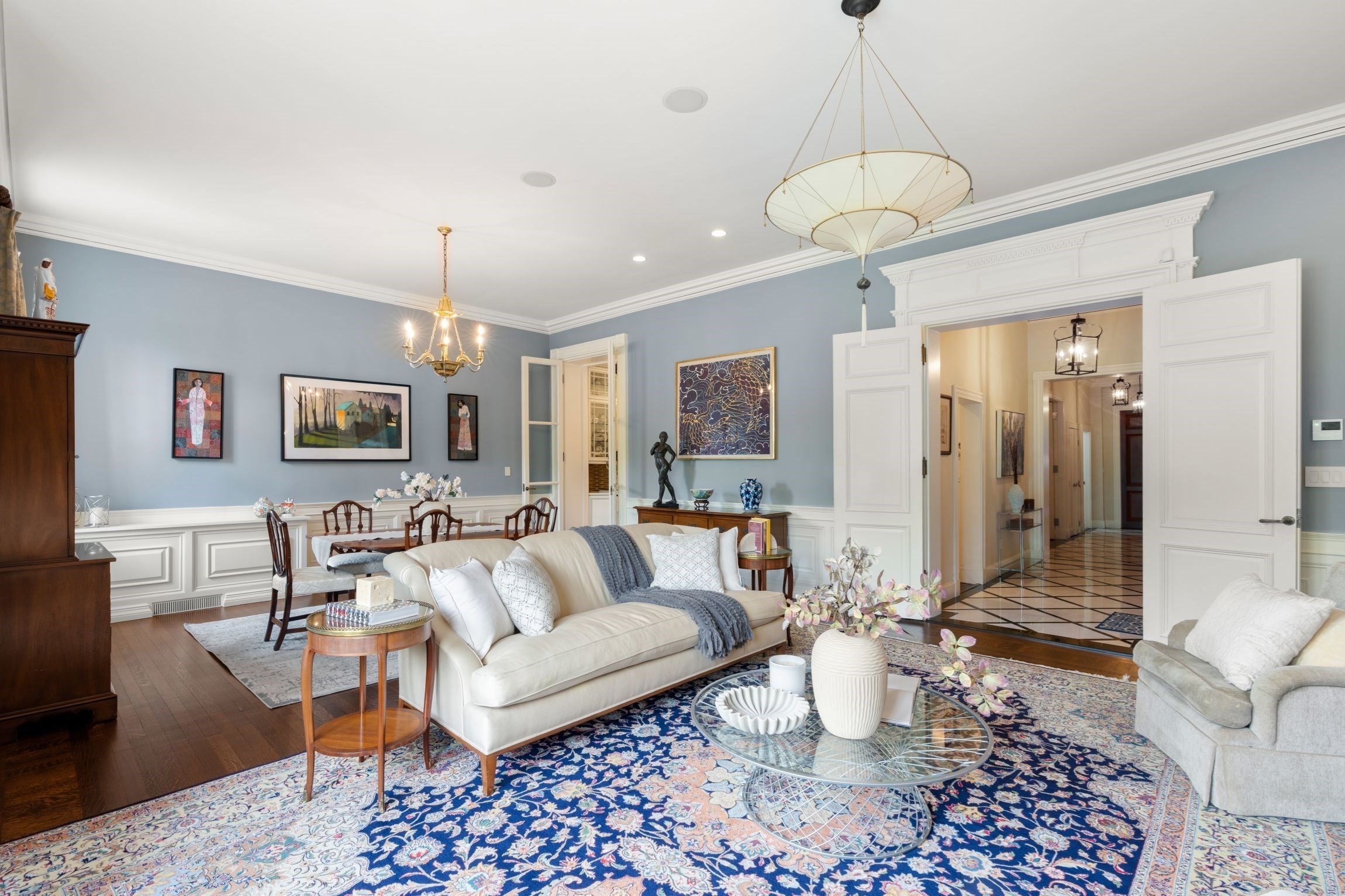 Living room with pale blue walls, white paneled trim, cream sofa, and ornate blue rug.