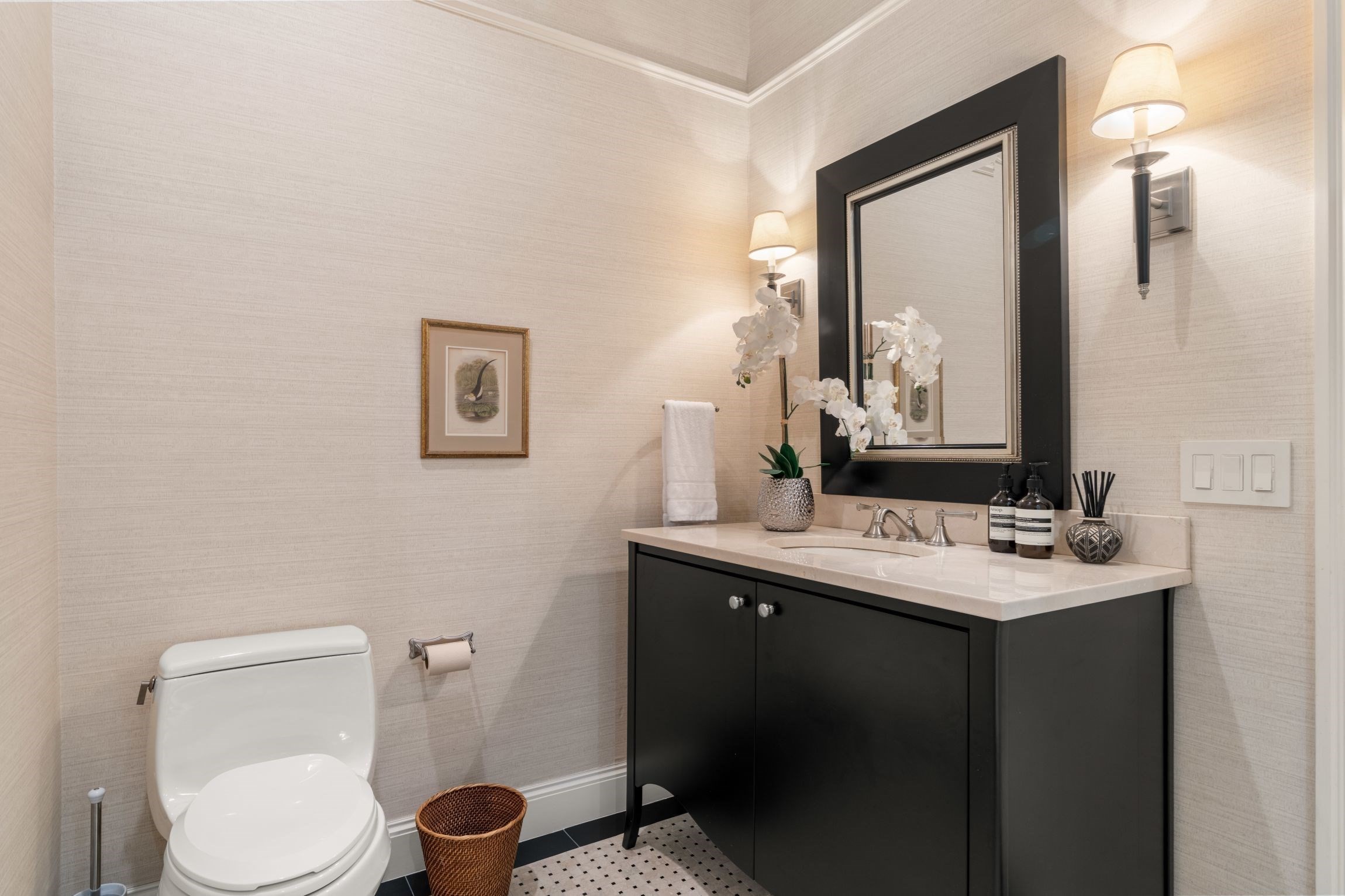 Bathroom with black vanity, large mirror, white orchid, and black-and-white floor tile.