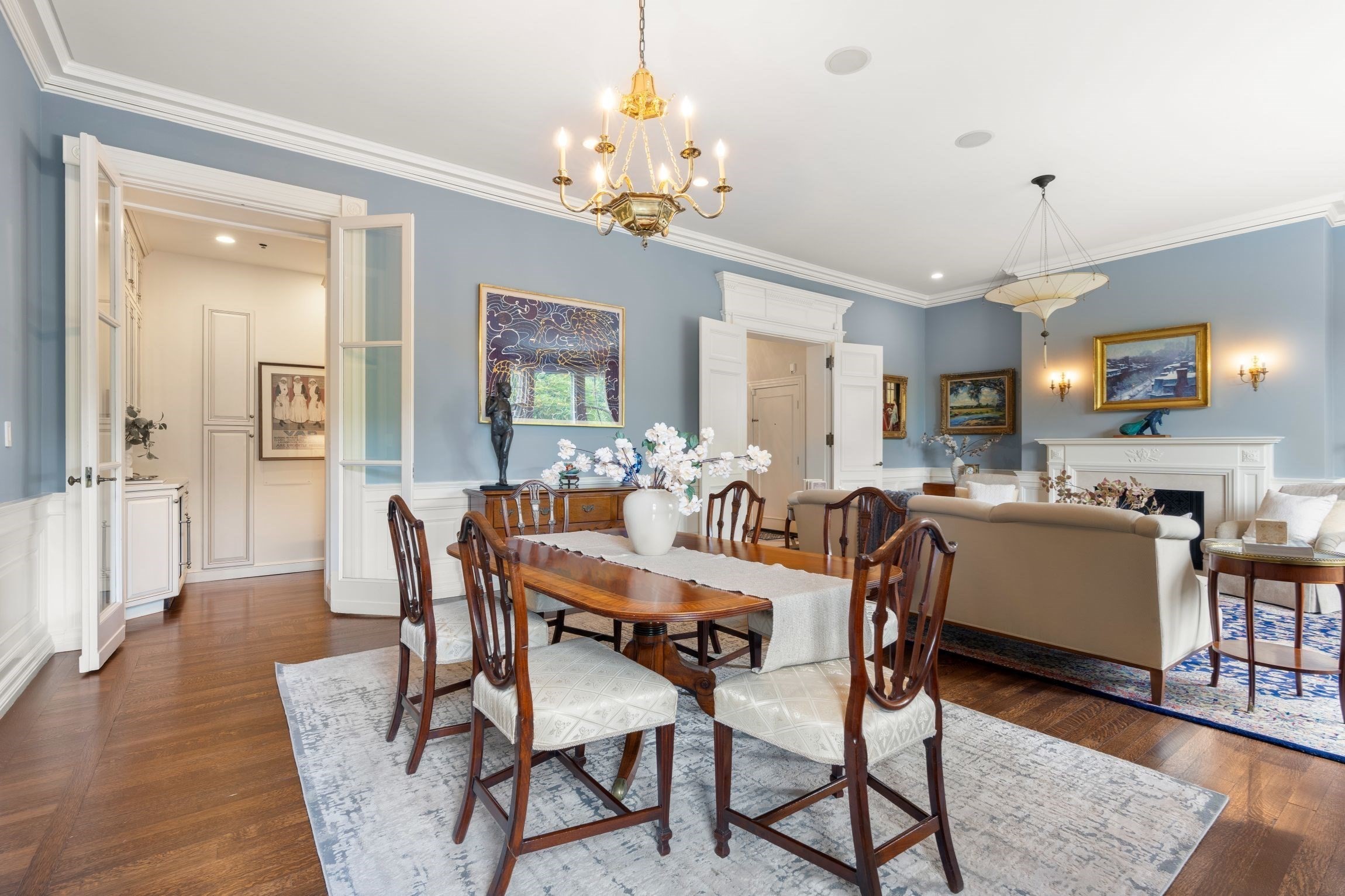 Dining room with a wood table and chandelier, opening into a living room with a fireplace.