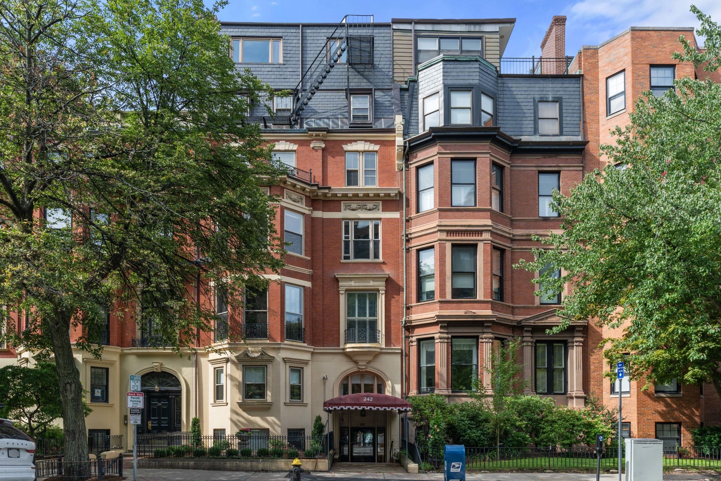 Red-brick apartment building at 242 Beacon Street, with ornate bay windows, slate roof and a burgundy entrance awning.