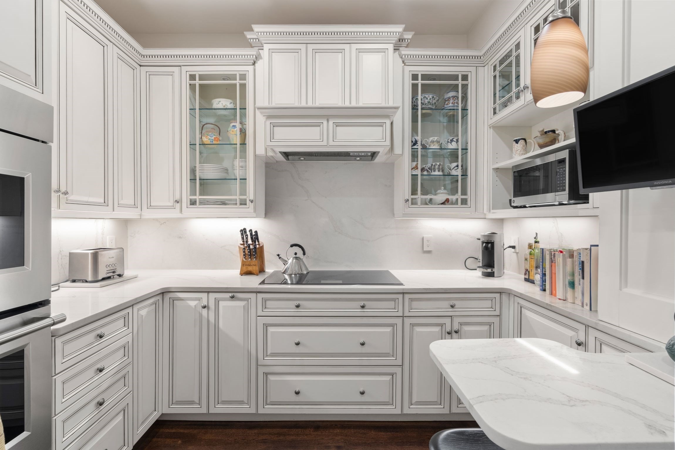 Kitchen with white paneled cabinets, marble counters, glass-front displays, and a large island.