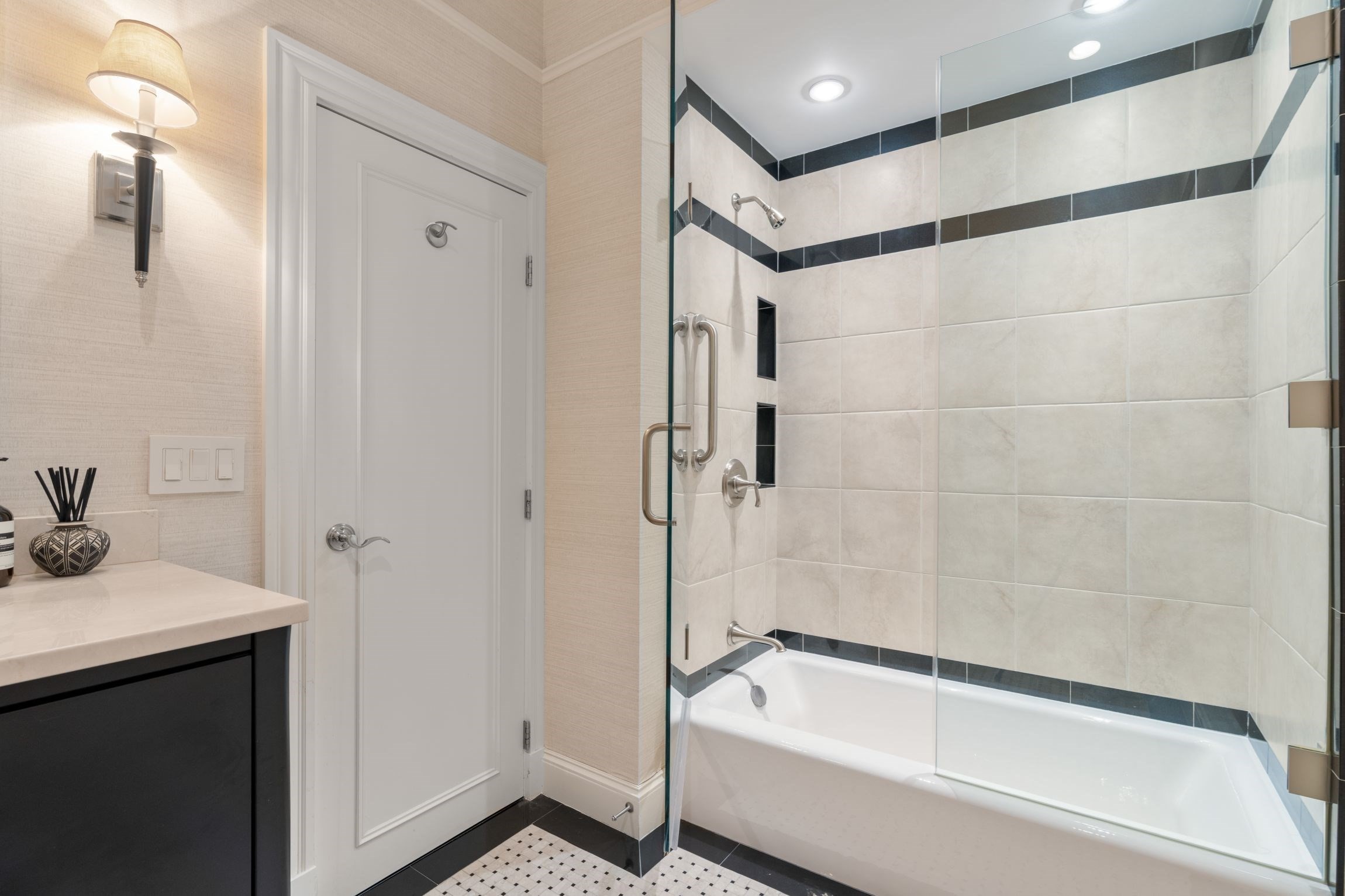 Bathroom with a glass-enclosed tub, dark tile accents, and a dark vanity.