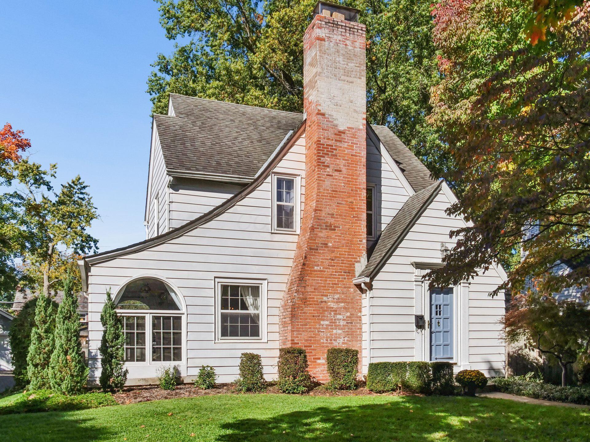 White-sided home with a tall brick chimney, blue front door, and large arched window.