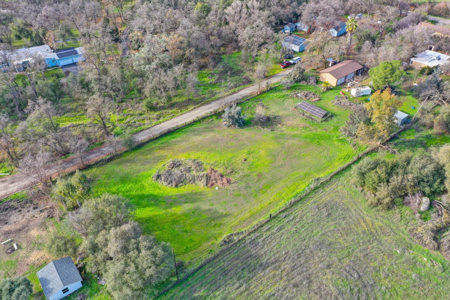 Aerial view of a green rural property with open land, scattered trees, outbuildings, and solar panels.