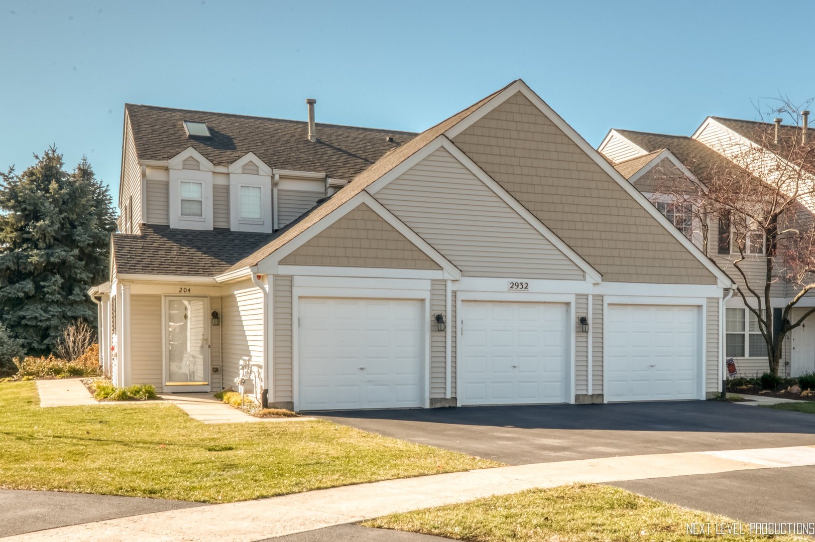 Beige attached townhome with three white garage doors and a covered entry.
