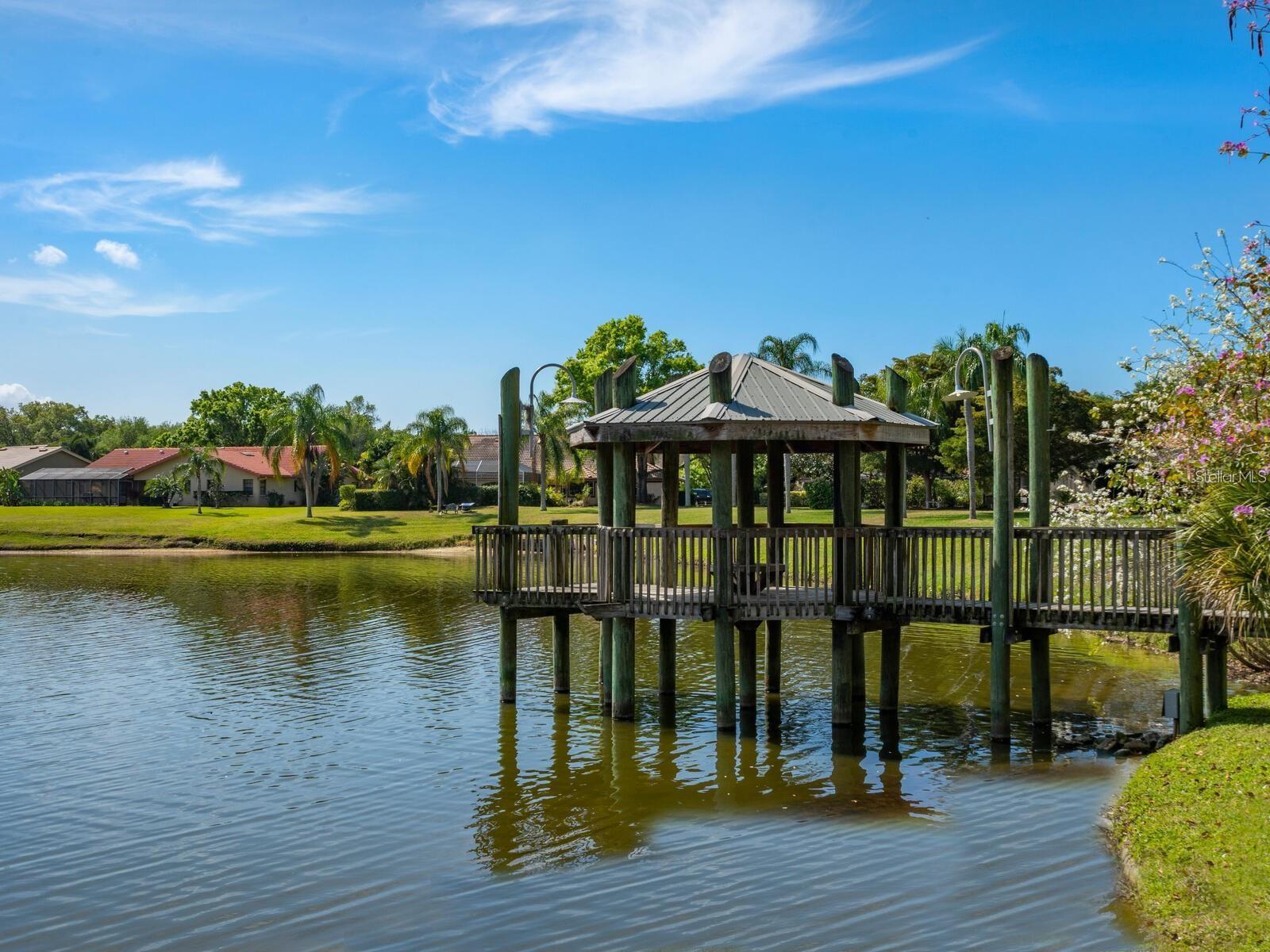 Covered wooden dock over a pond, with homes and palm trees across the water.