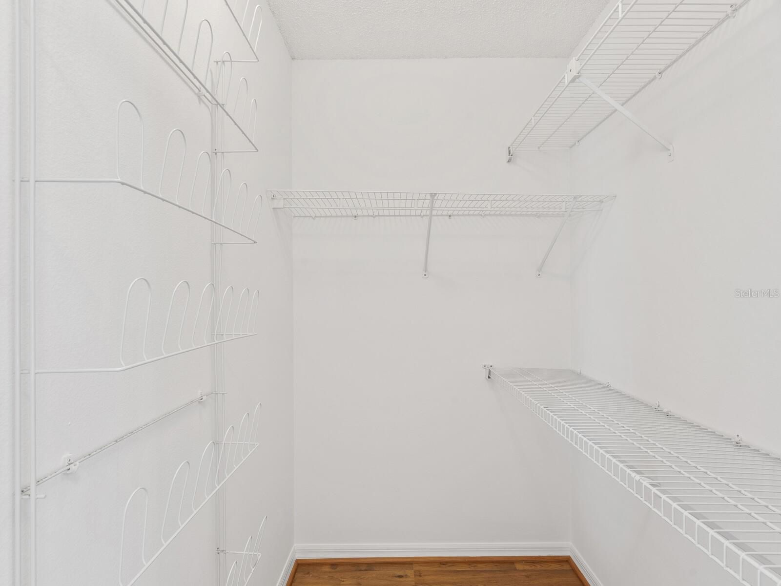 Walk-in closet with white wire shelving and hanging racks above a wood floor.