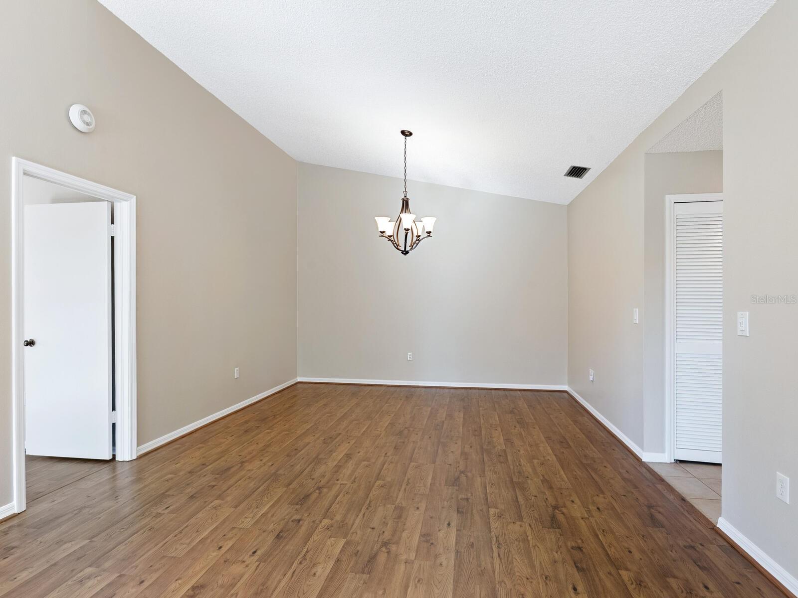 Empty dining room with wood-look flooring, vaulted ceiling, and hanging chandelier.