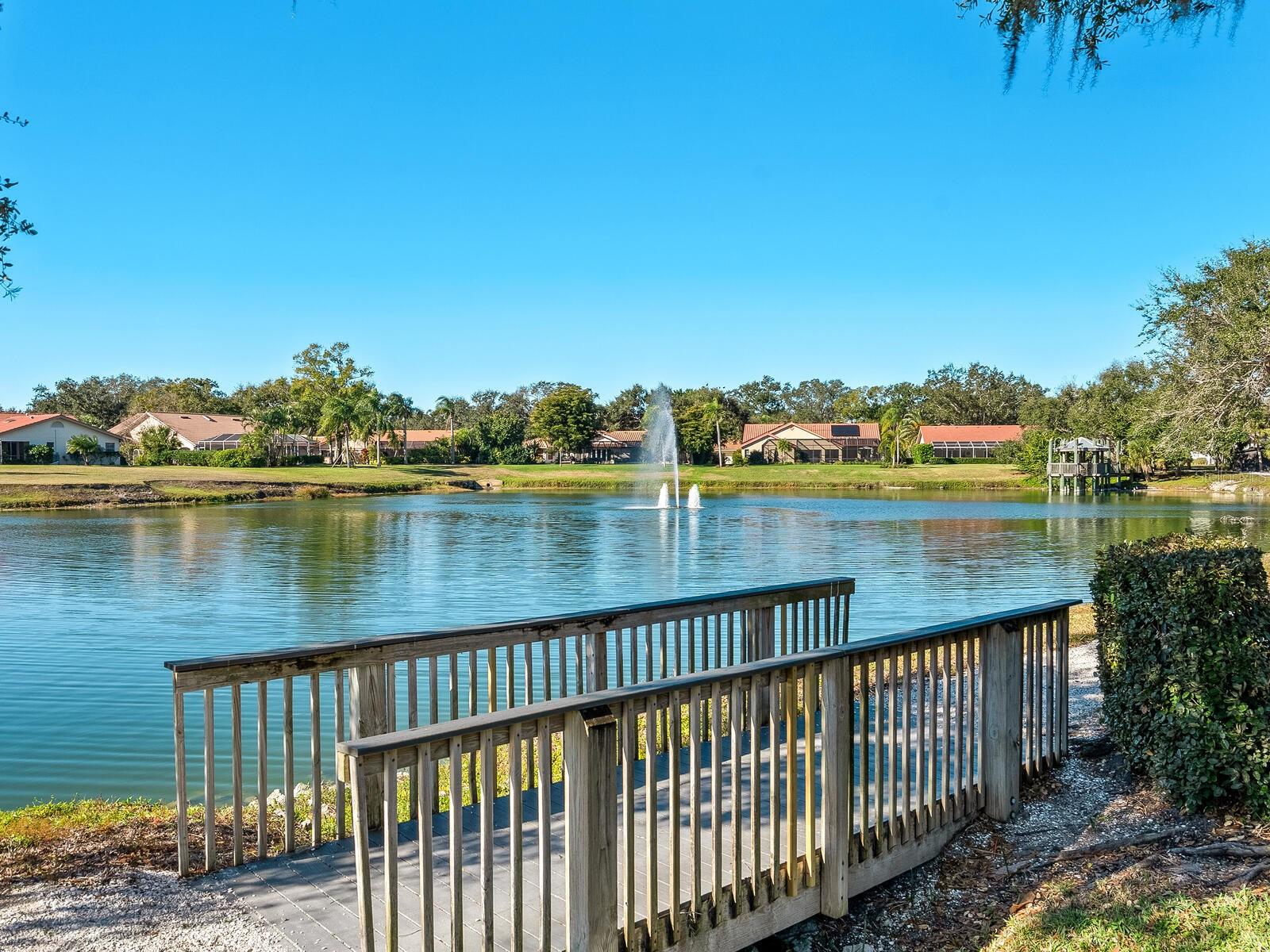 Community pond with fountain, viewed from a wooden ramp and railing.