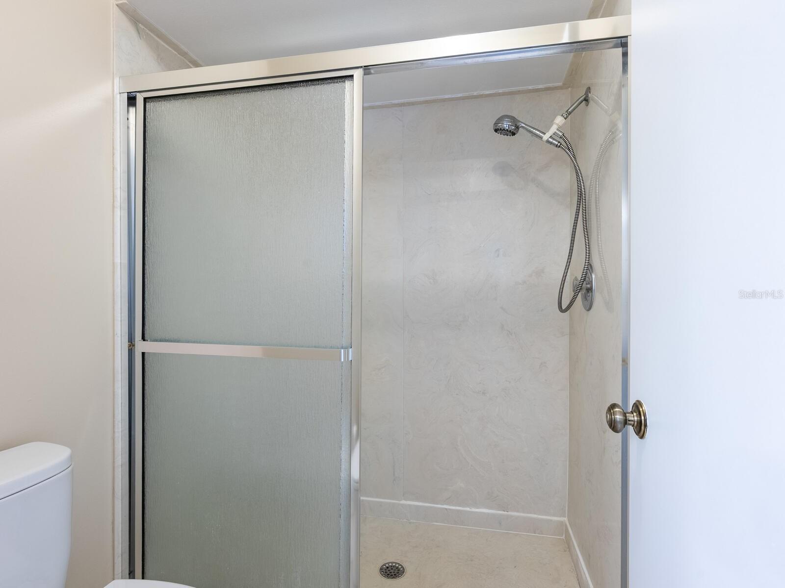 Bathroom shower with a frosted sliding-glass door, handheld showerhead, and light marble-look wall panels.