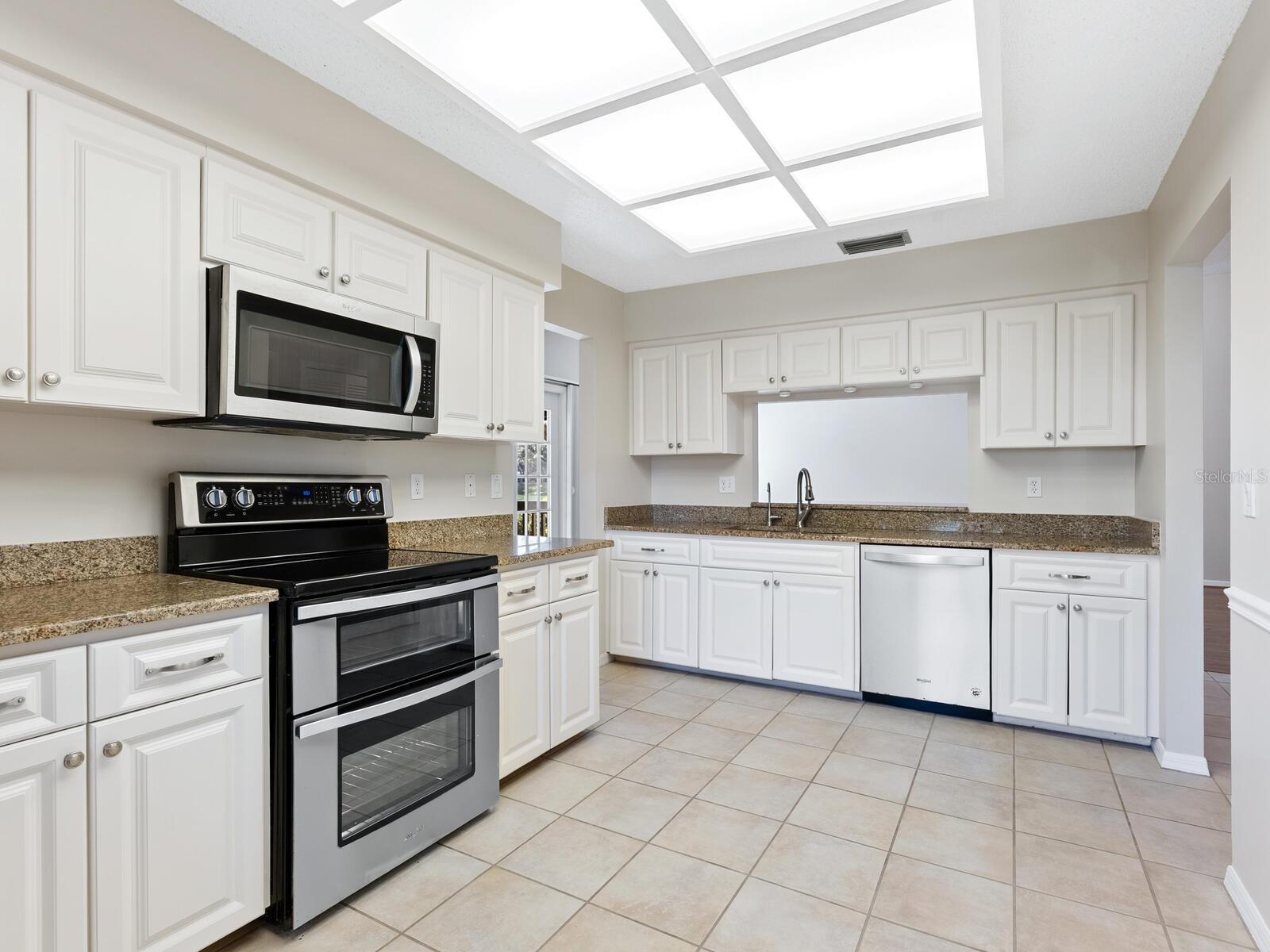 Kitchen with white cabinets, granite countertops, black-and-stainless appliances, and large tile flooring.