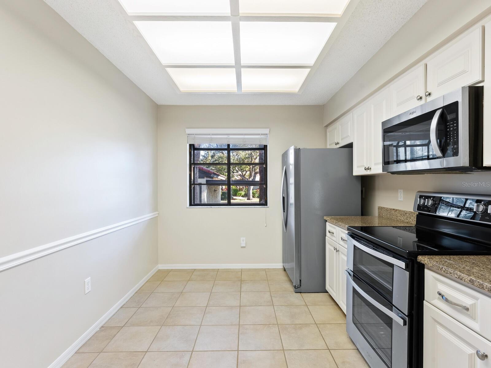 Kitchen with white cabinets, stainless steel appliances, granite counters, and a large illuminated ceiling panel.