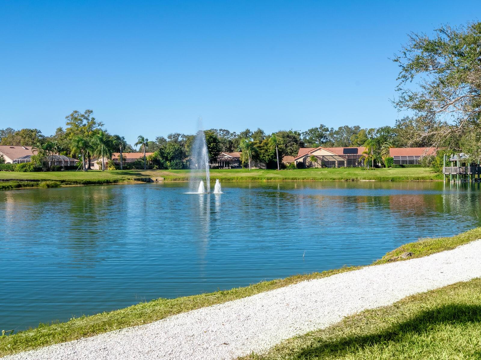 Community pond with a central fountain, homes along the far bank, and a gravel path.