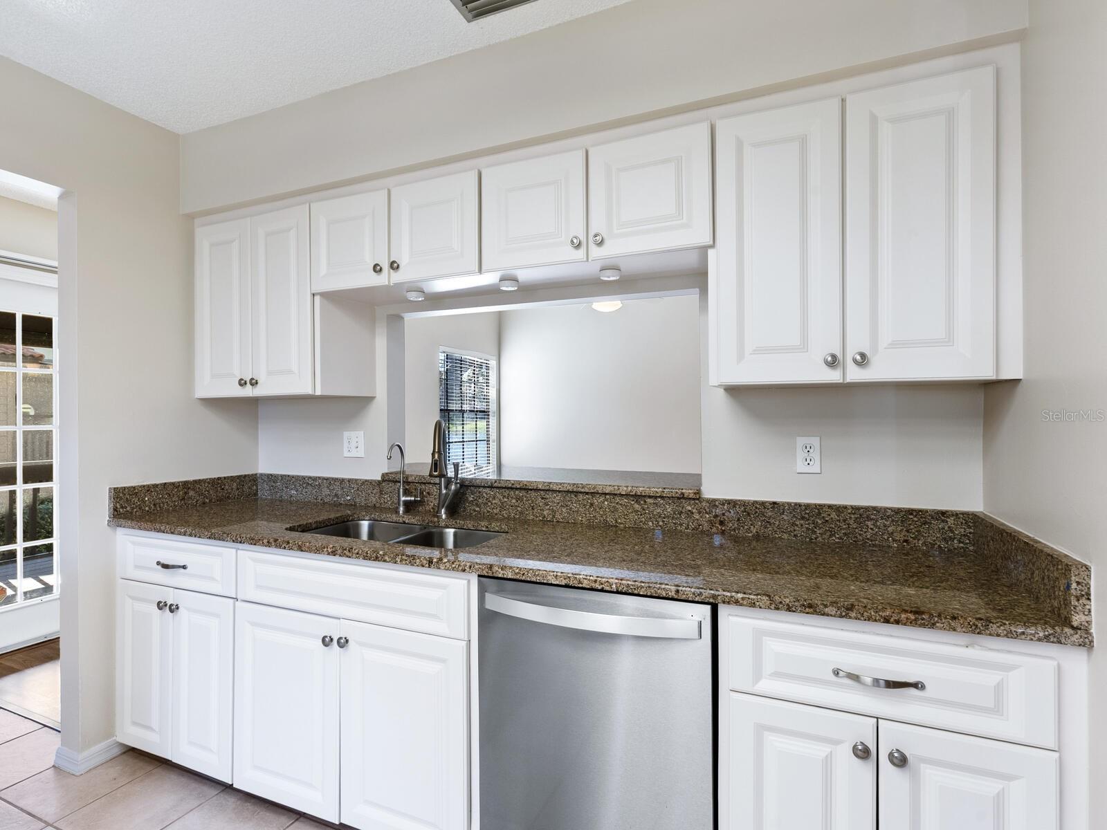Kitchen with white cabinets, brown granite counters, double sink, and stainless steel dishwasher.