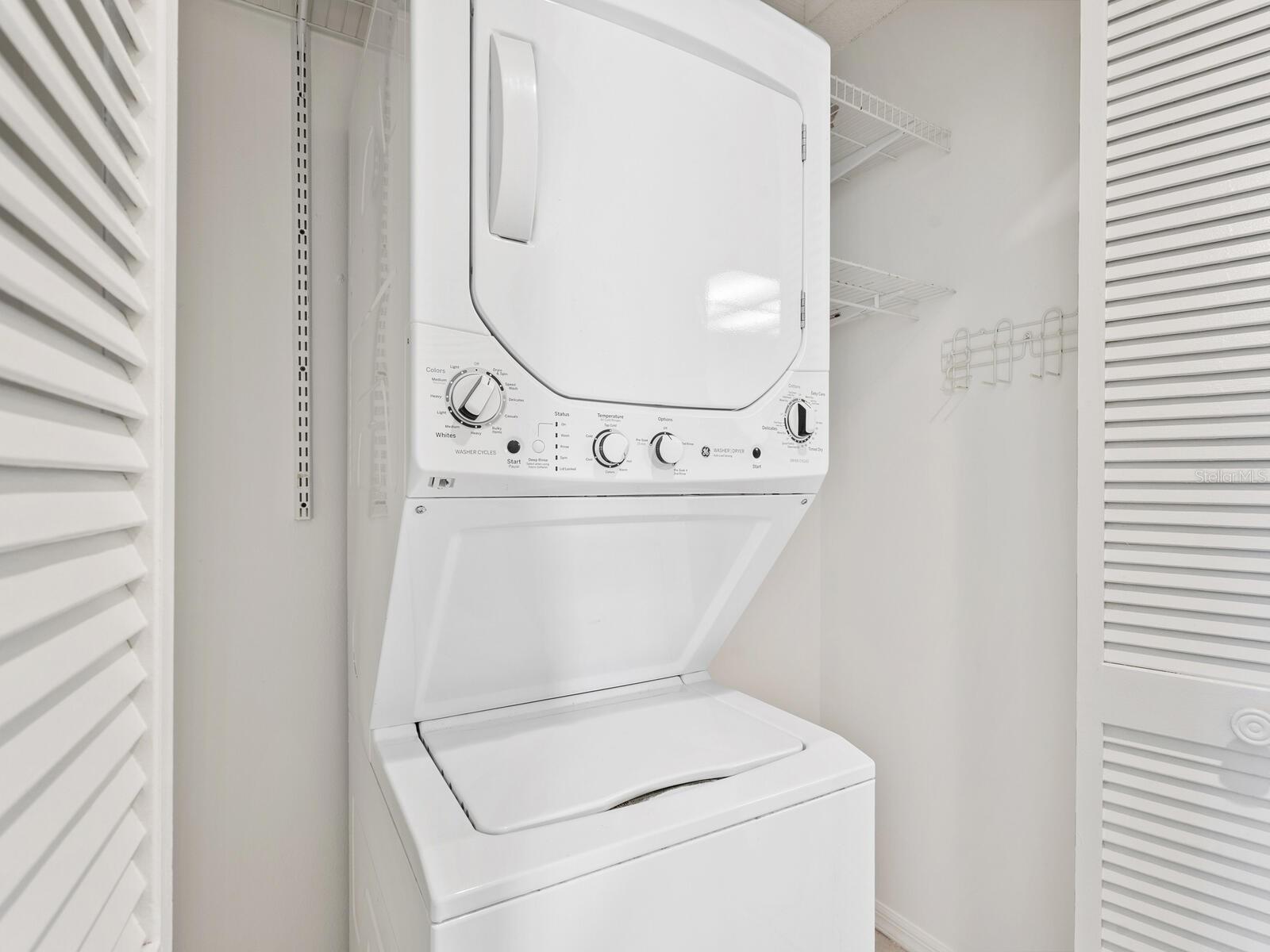 Stacked white washer and dryer in a laundry closet with wire shelving and hanging hooks.