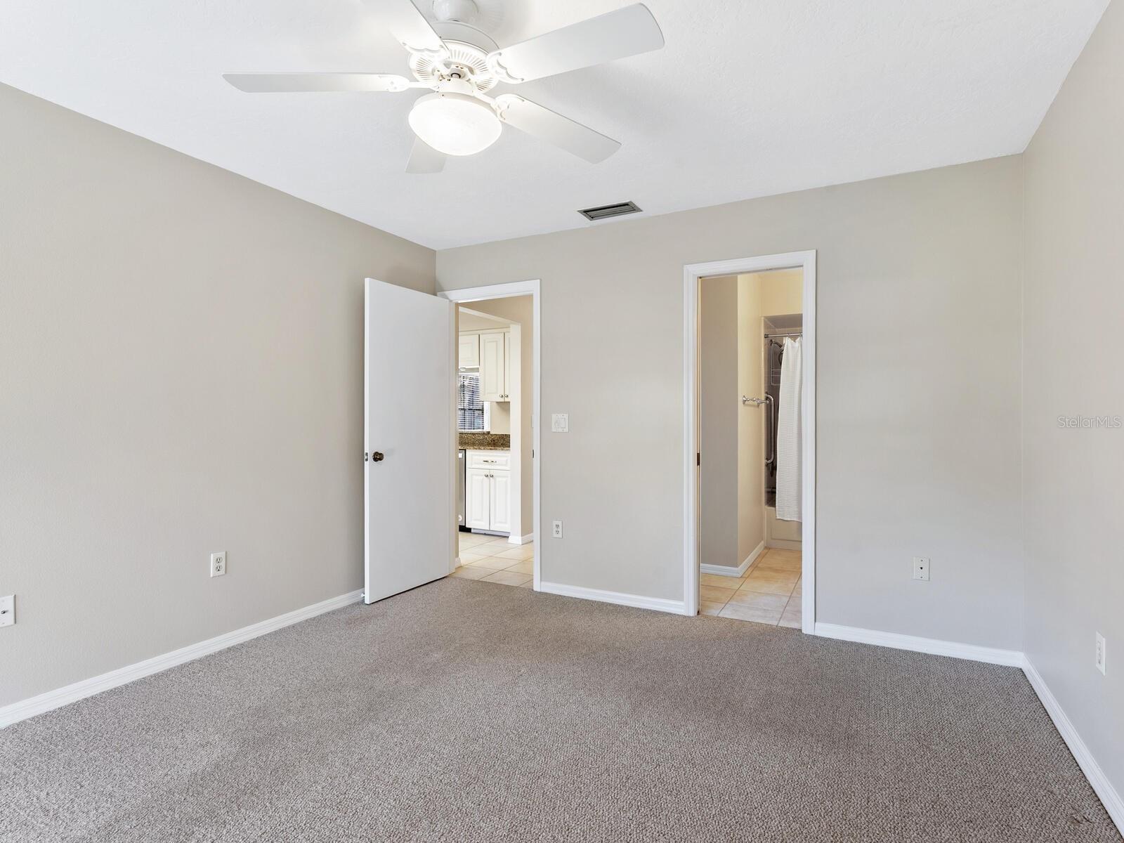 Unfurnished carpeted bedroom with a ceiling fan and doorways to the kitchen and bathroom.