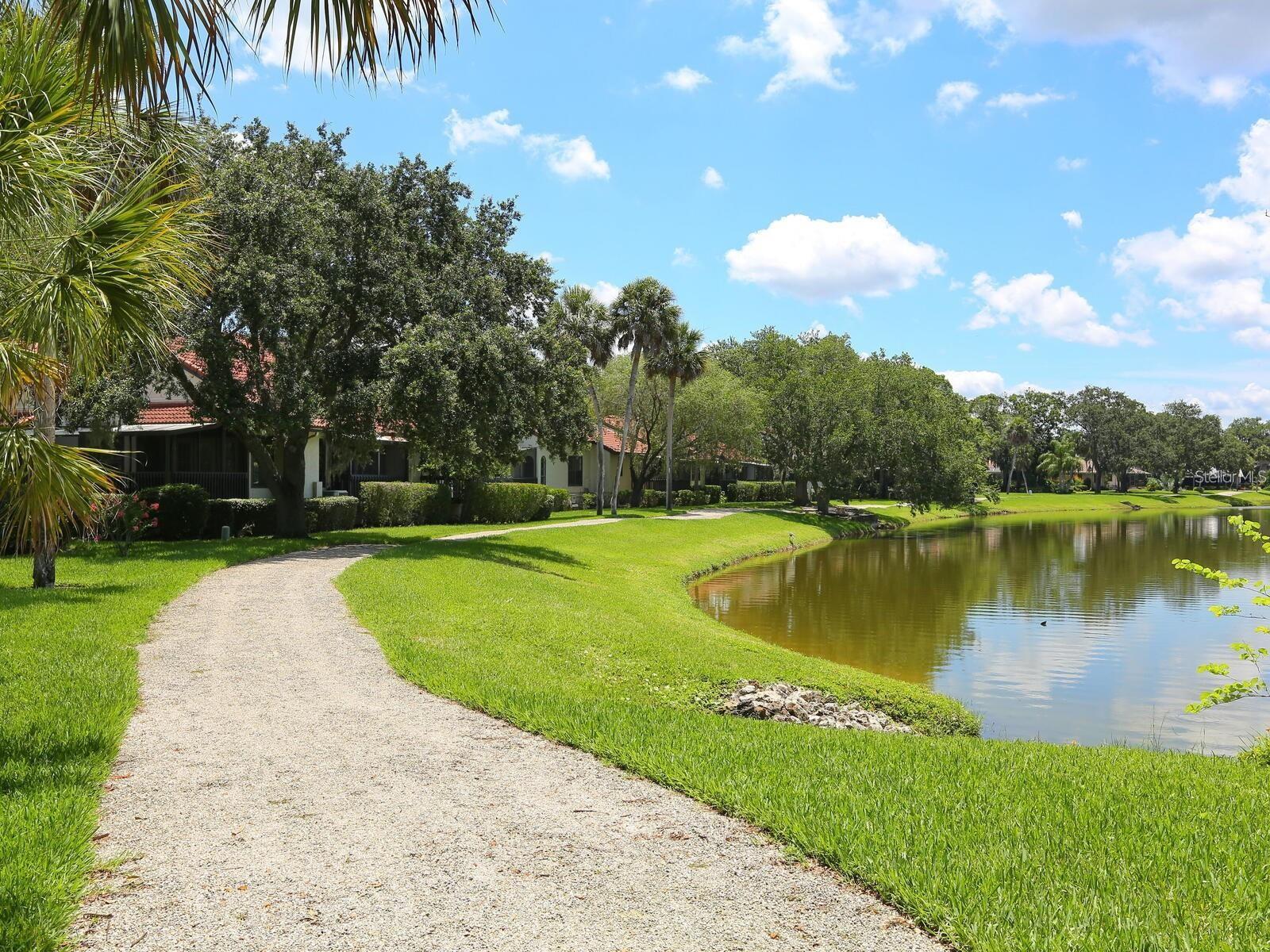 Condominiums beside a pond, with a curved gravel path and palm trees.