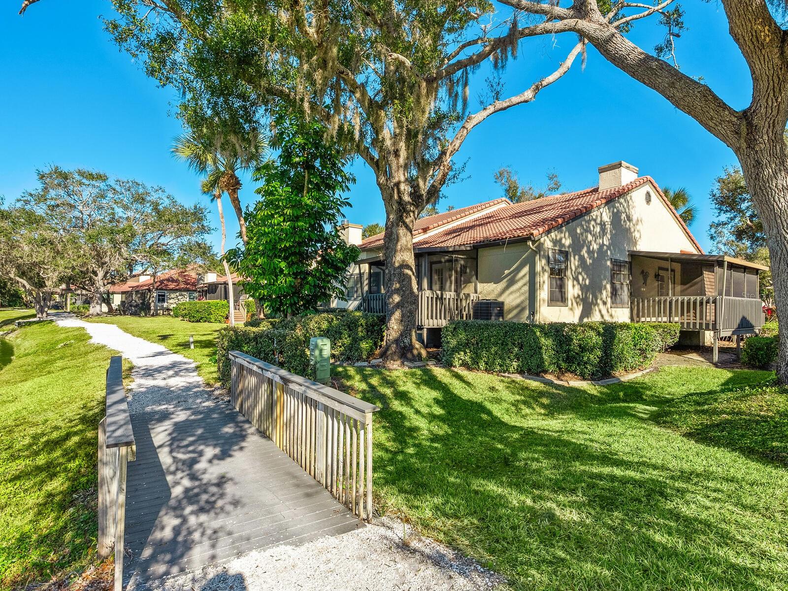 One-story home with a red tile roof and screened porch, reached by a walkway under large shade trees.
