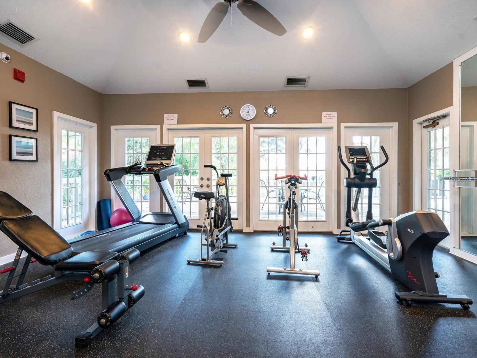 Fitness room with treadmills, stationary bikes, and an elliptical beside tall windows and French doors.