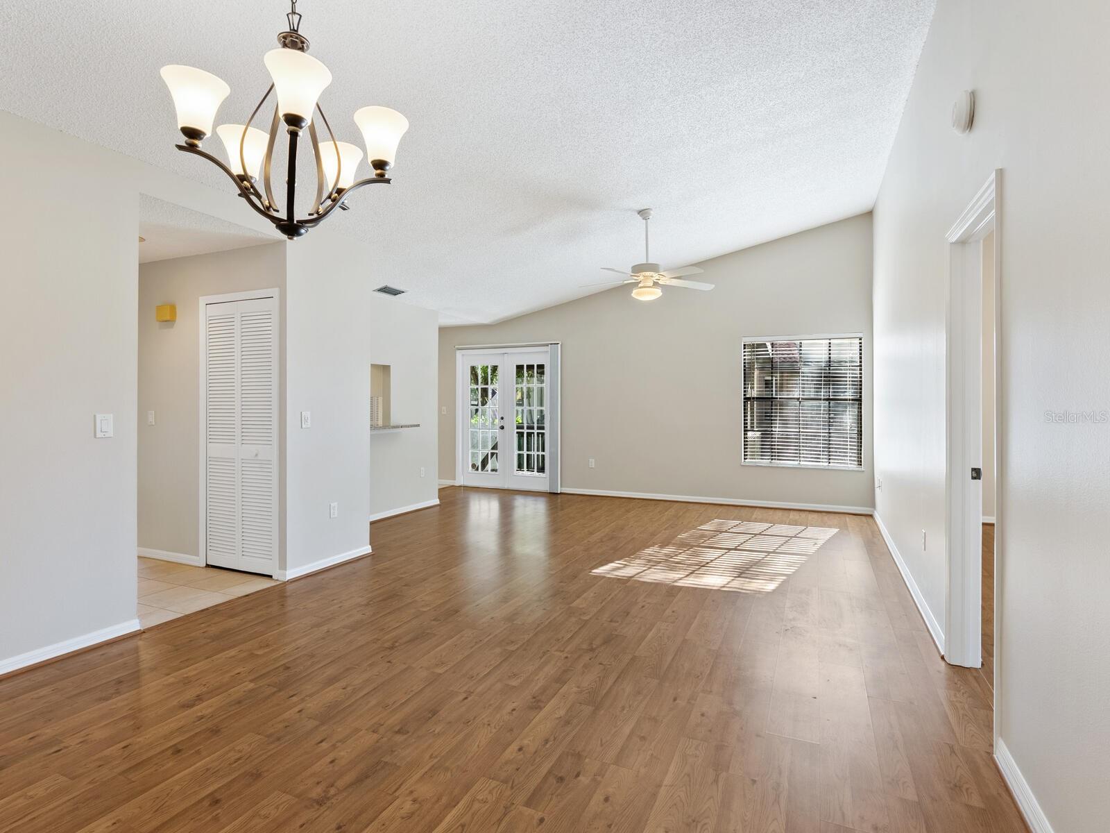 Empty living room with hardwood floors, a chandelier, and French doors.