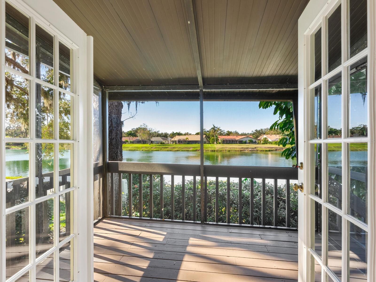 Screened porch with a lake view, wood-plank ceiling, and open French doors.