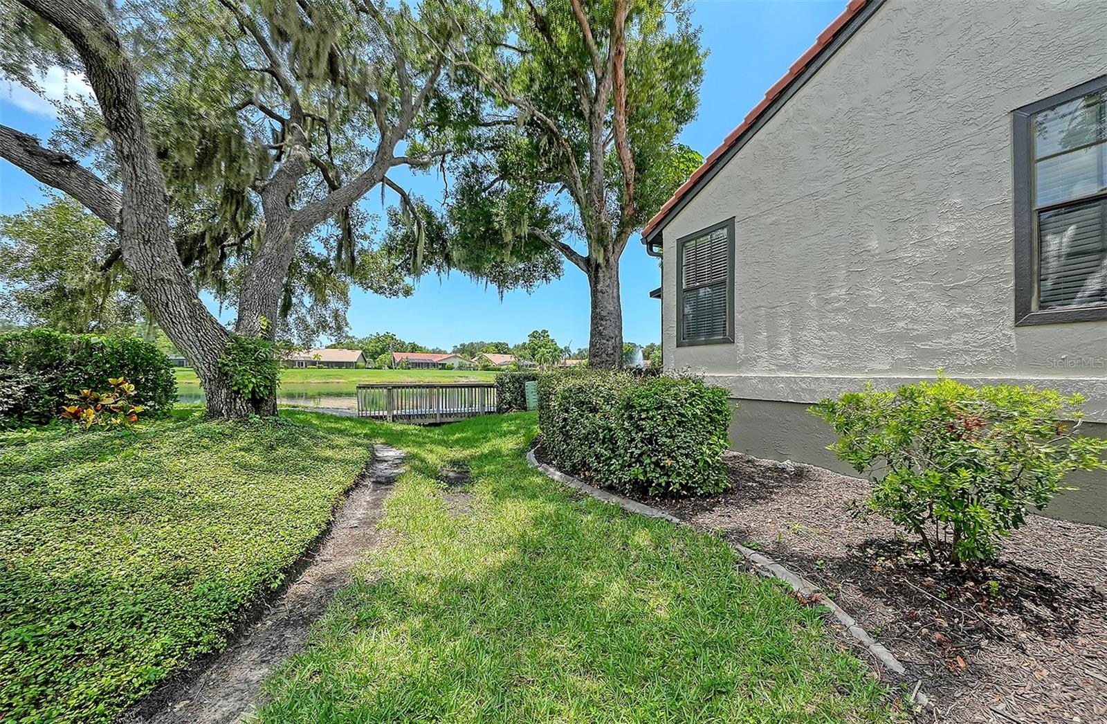 Home exterior beside a pond, with mature oak trees, landscaped grounds, and a small dock.