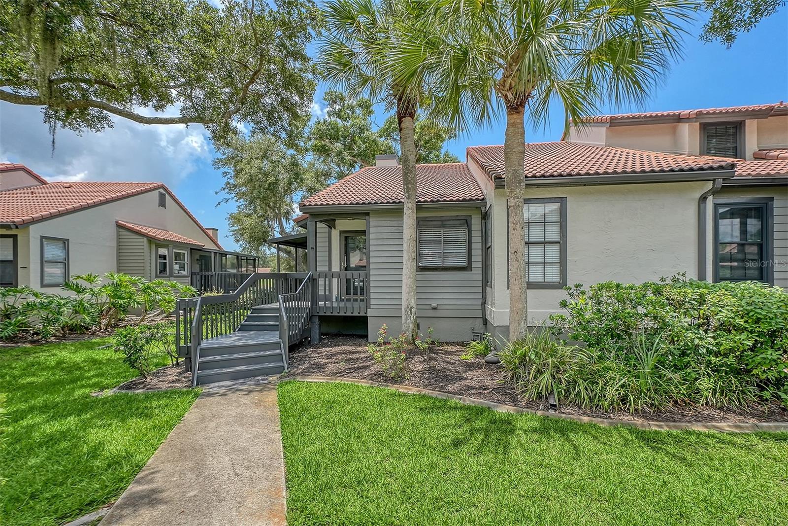 Home exterior with a raised entry ramp, red tile roof, and palm trees.