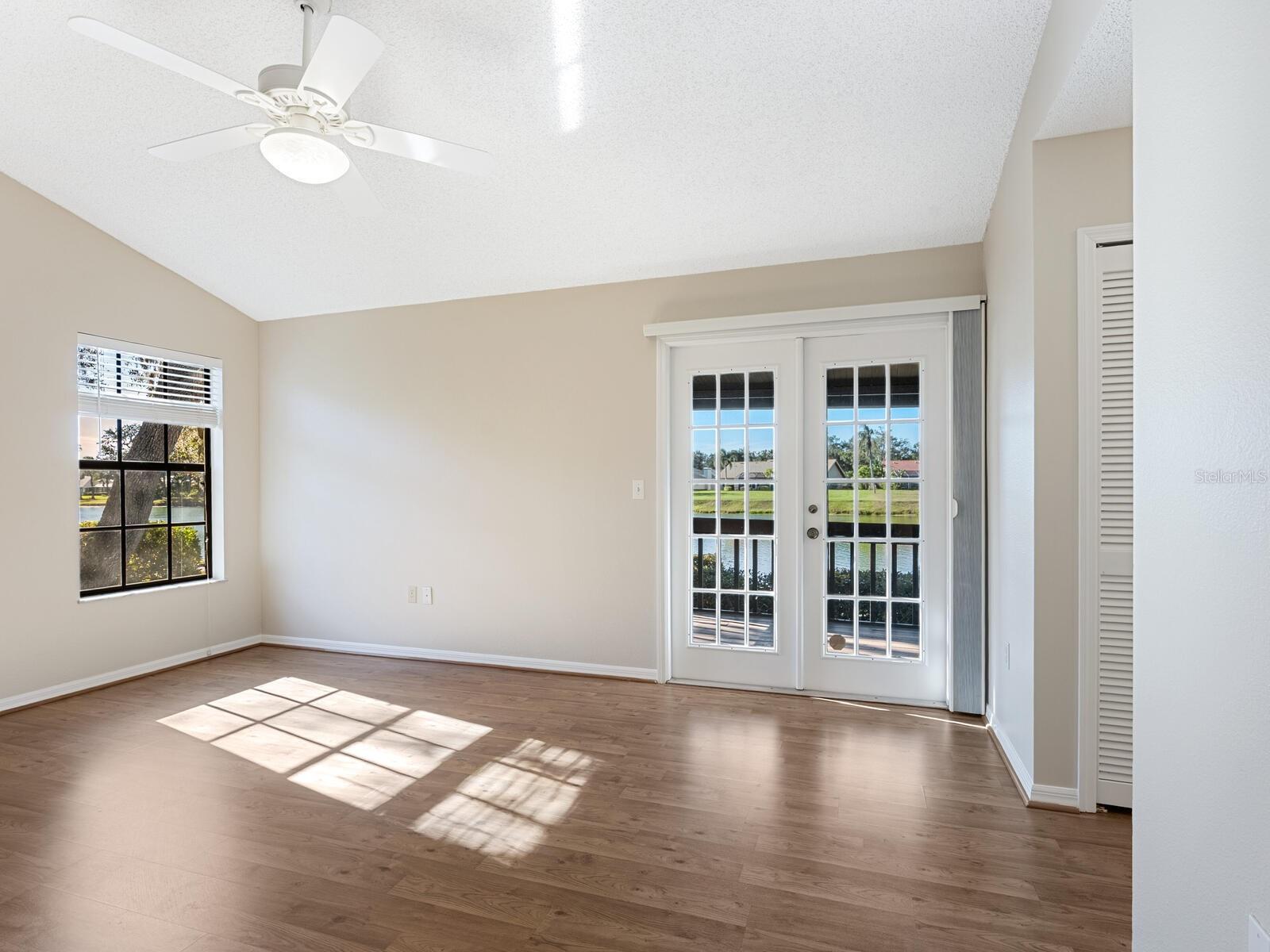 Vacant living room with wood flooring and French doors overlooking the water.