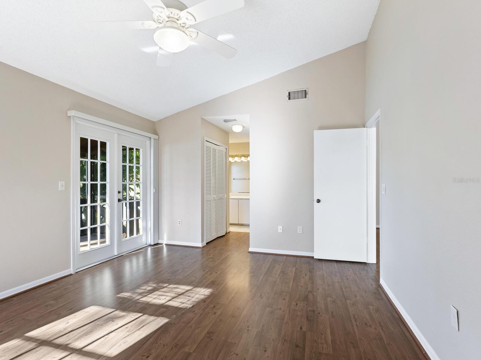 Empty bedroom with wood floors, French doors, and a ceiling fan.