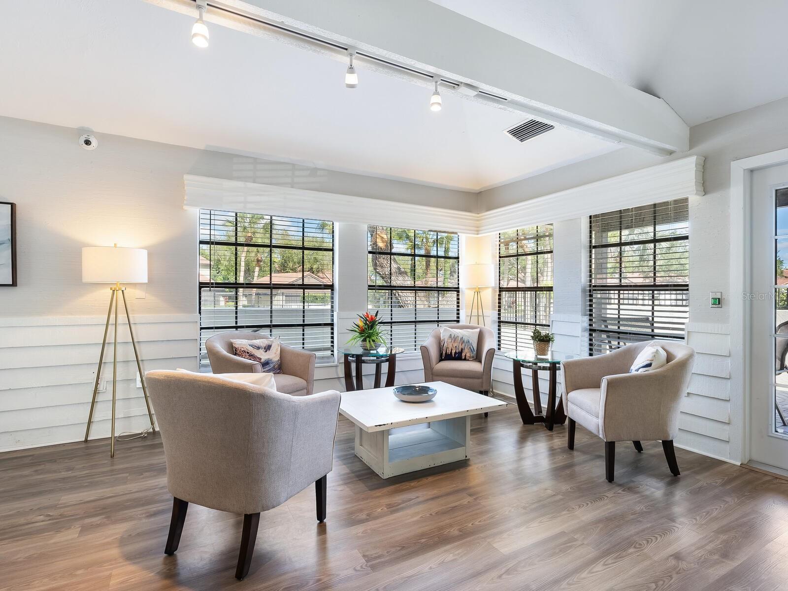 Staged living room with four armchairs, a white coffee table, and large windows with dark blinds.