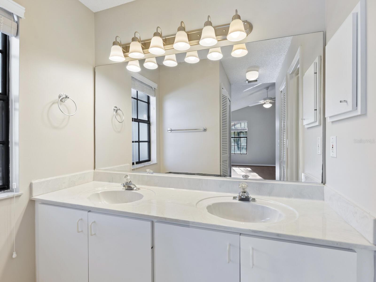 Bathroom with a double-sink white vanity, large mirror, and a row of lights above it.