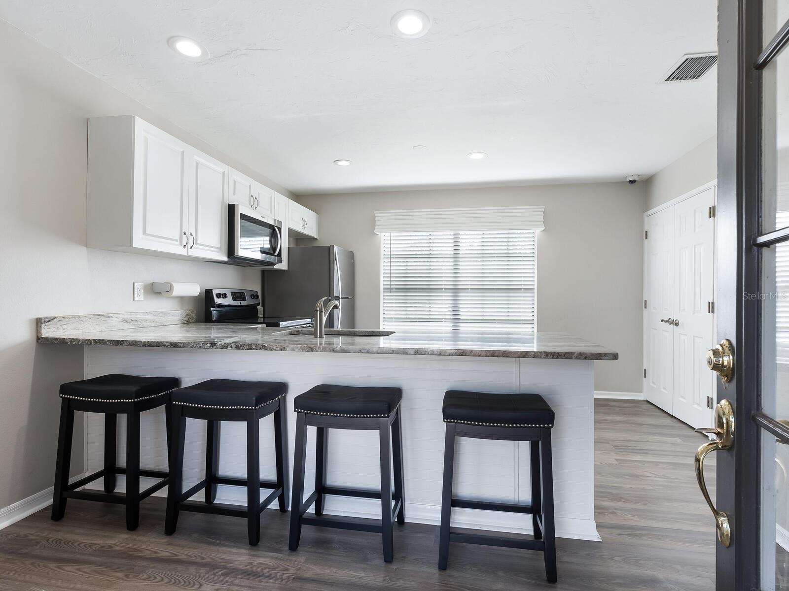 Kitchen with white cabinetry, a long breakfast bar, four black stools, and stainless steel appliances.
