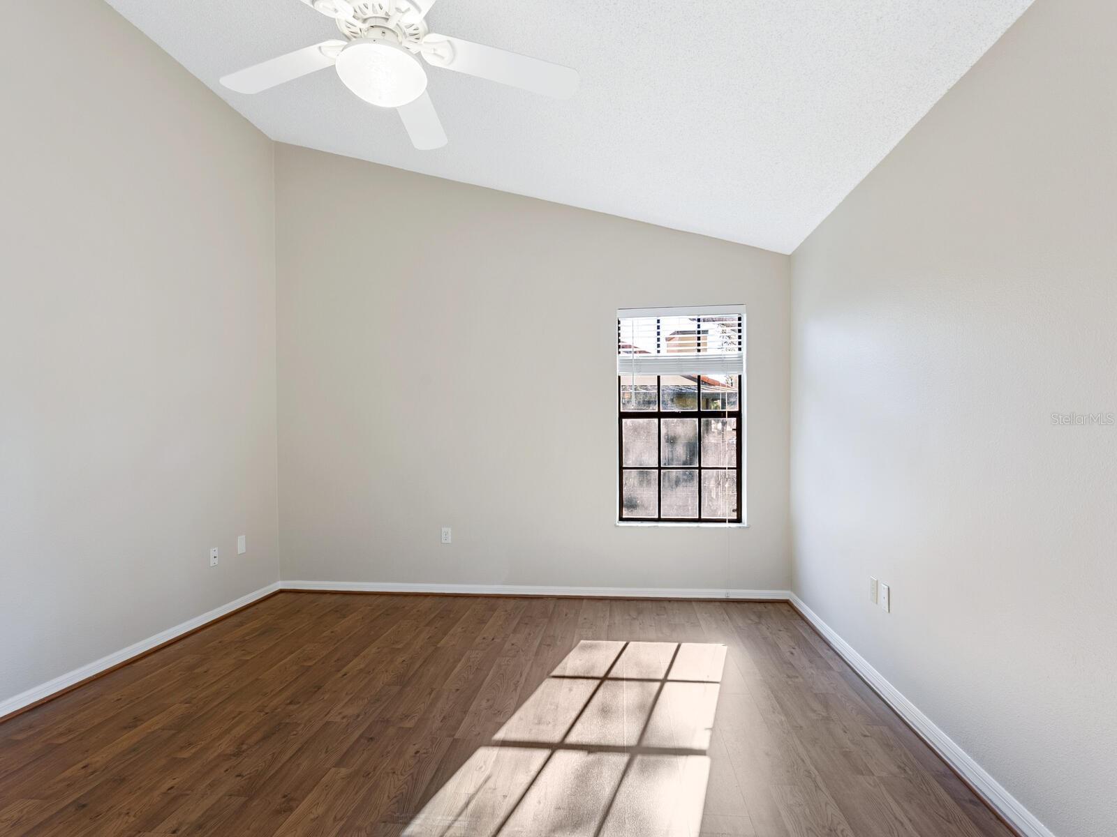 Empty room with wood-look flooring, a ceiling fan, and sunlight through a window.