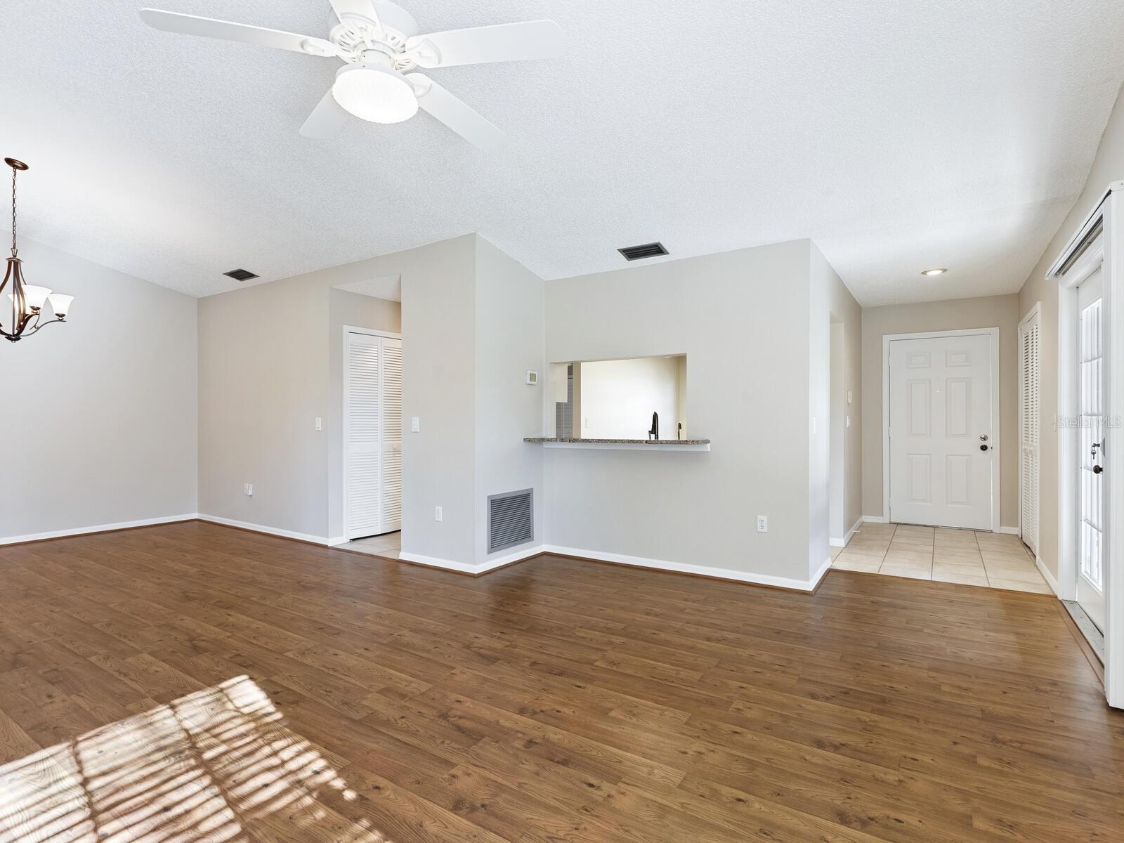 Vacant living area with wood floors, a kitchen pass-through, and sunlight streaming through glass doors.