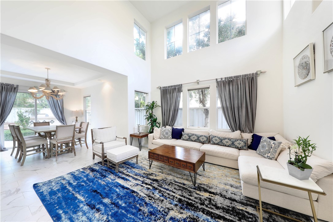 Living and dining room with a double-height ceiling, cream sectional, and blue patterned rug.
