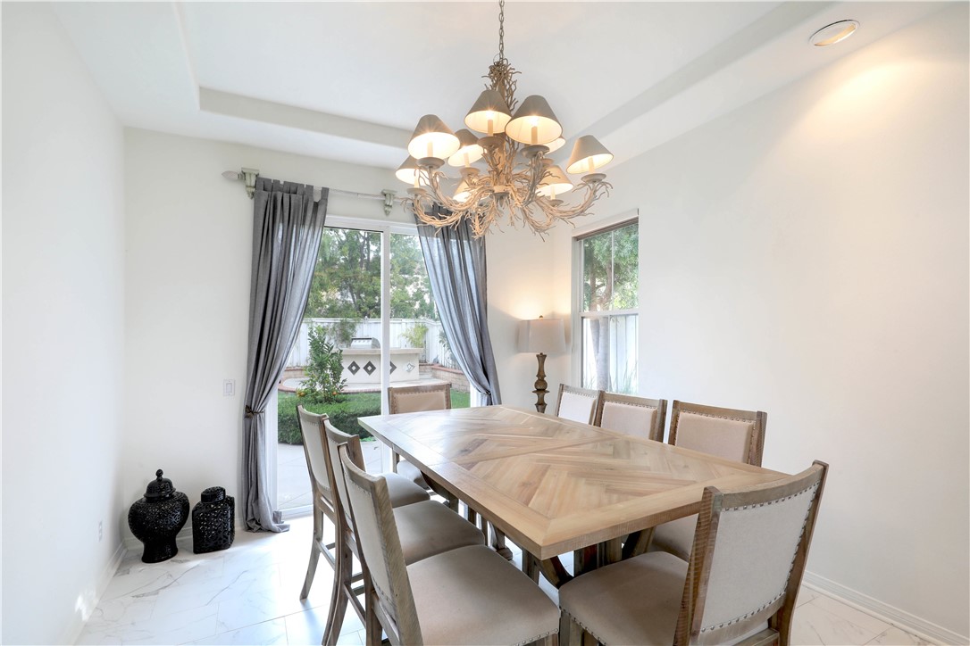 Dining room with a long wood table, ornate chandelier, and glass doors opening to a garden patio.
