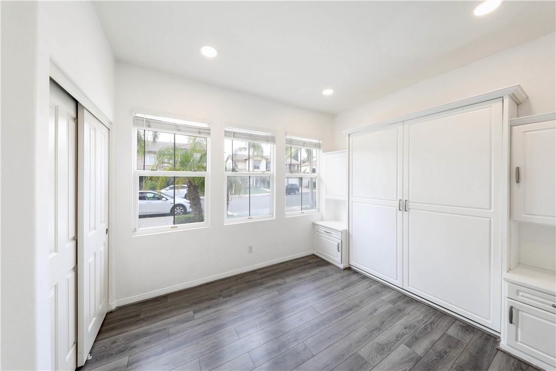 Empty room with white built-in cabinets, gray flooring, and three street-facing windows.