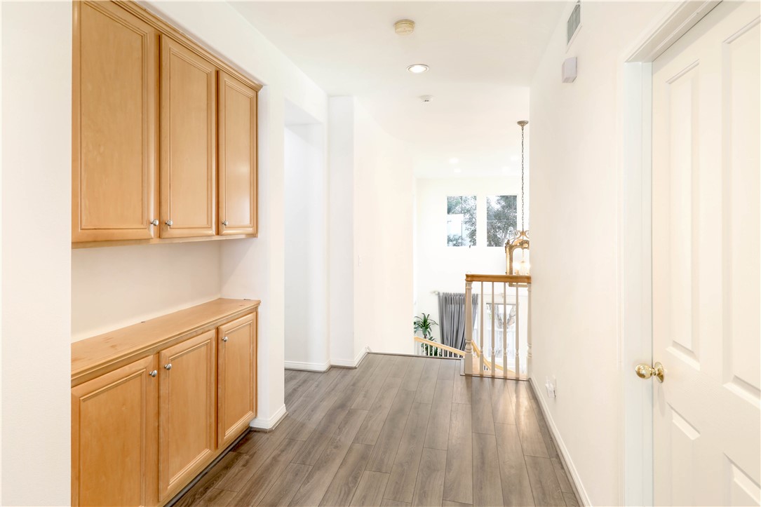 Upstairs hallway with built-in wood cabinets, gray flooring, and a railing overlooking the stairs.