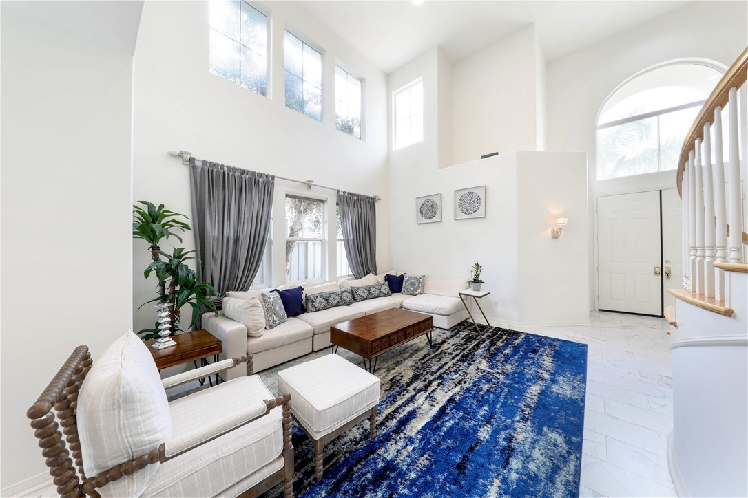 Furnished living room with a double-height ceiling, tall windows, and a blue patterned rug.