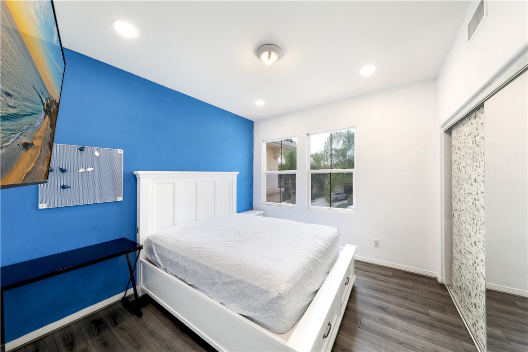 Bedroom with a white bed, blue accent wall, and windows overlooking greenery.