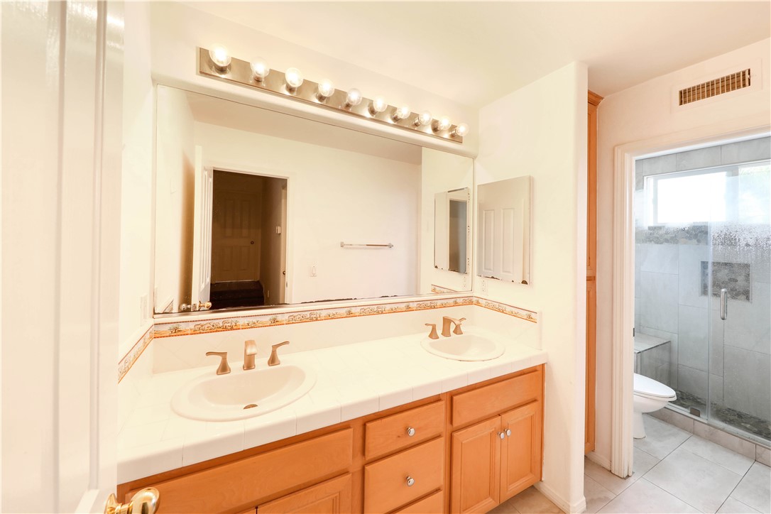 Bathroom with a double-sink vanity, wood cabinetry, and an adjoining glass-enclosed shower.
