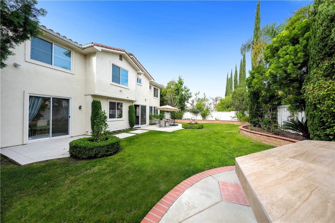 Backyard with a broad lawn, paved patio, outdoor dining set, and landscaped garden beds.