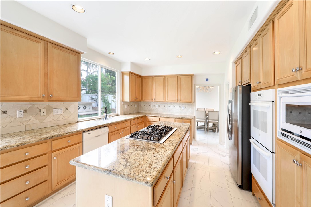 Kitchen with a granite island and gas cooktop, wood cabinetry, and double wall ovens.