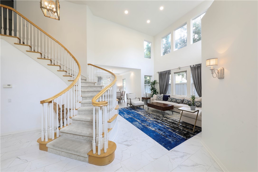 Two-story living room with a curved staircase, tall windows, and a blue rug.
