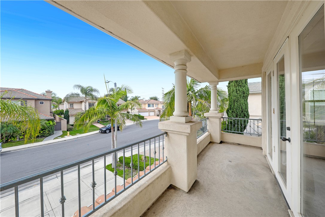 Covered balcony with stucco columns and metal railing overlooking a palm-lined residential street.