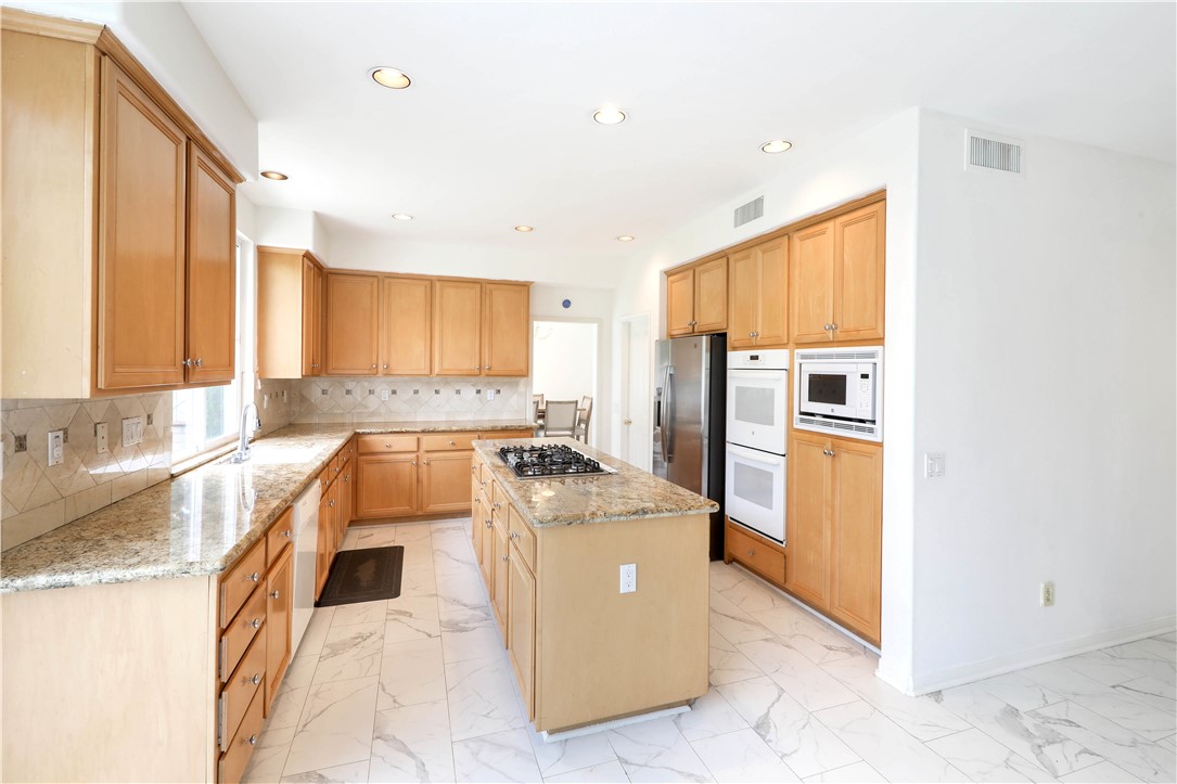 Kitchen with wood cabinetry, granite counters, central cooktop island, and built-in ovens.