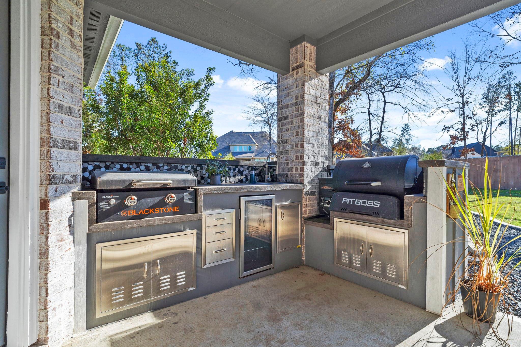 Covered patio outdoor kitchen with Blackstone griddle, Pit Boss smoker, and stainless-steel cabinets.