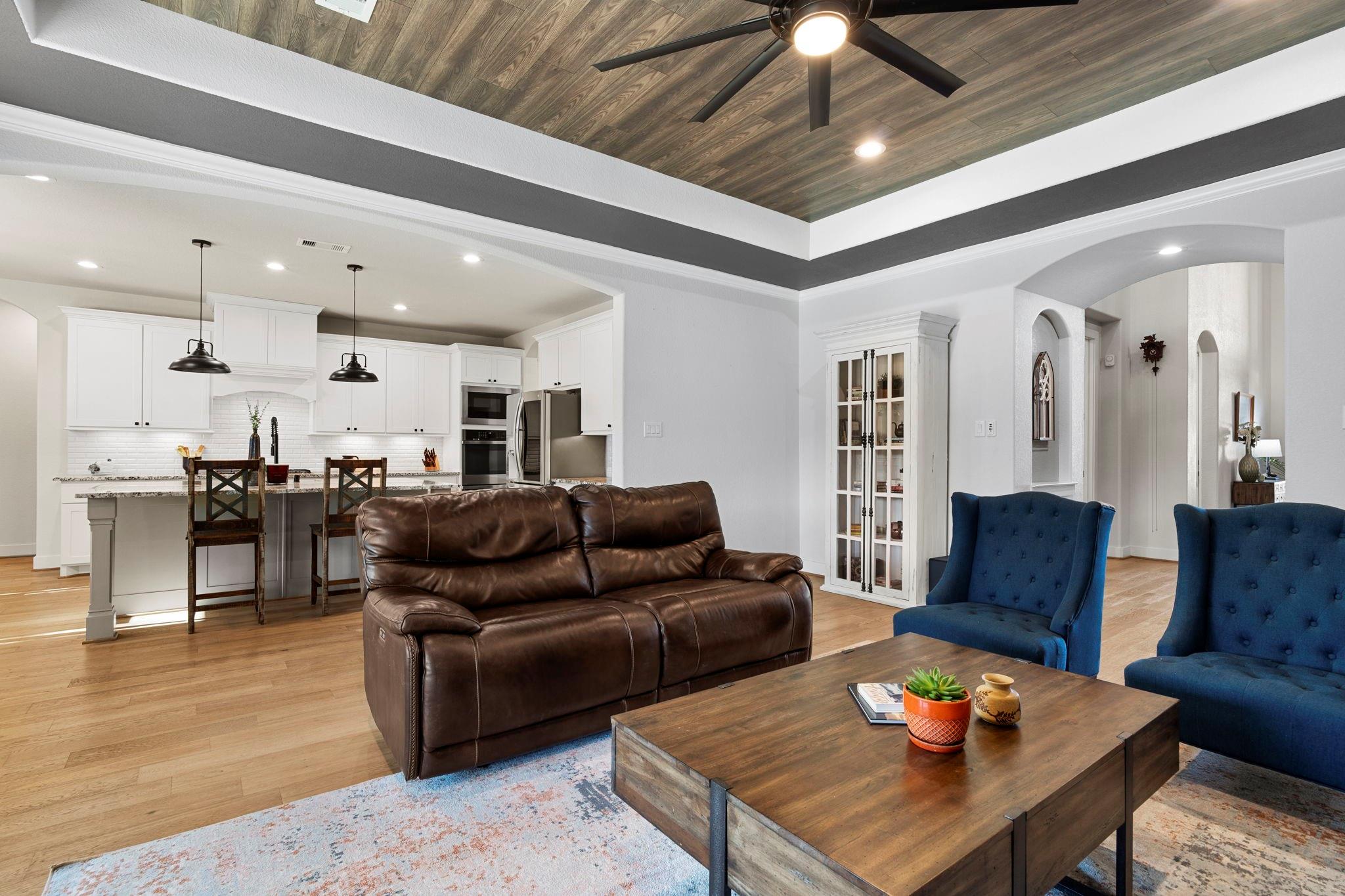 Open-plan living room with a leather sofa, blue armchairs, and a wood-paneled ceiling.