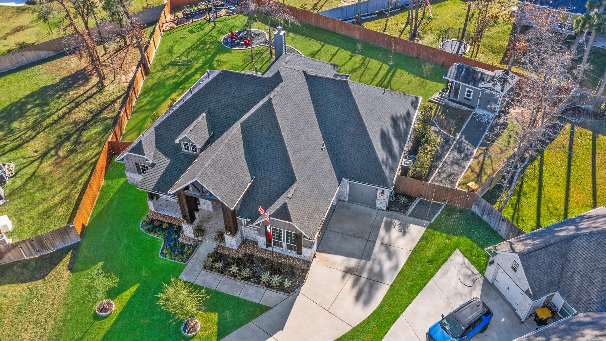Aerial view of a gray-roofed home and fenced lawn with a backyard play area and detached outbuilding.
